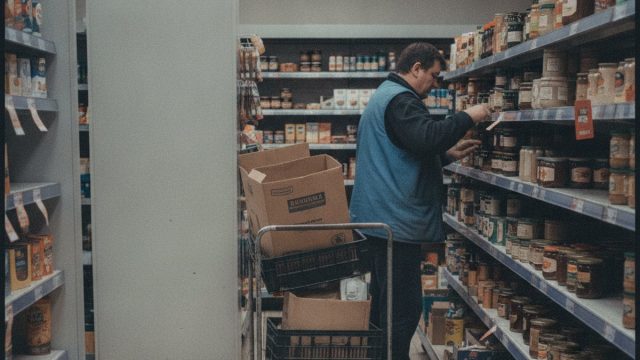 Pracownik sklepu uzupełnia towar na półkach w sklepie spożywczym
